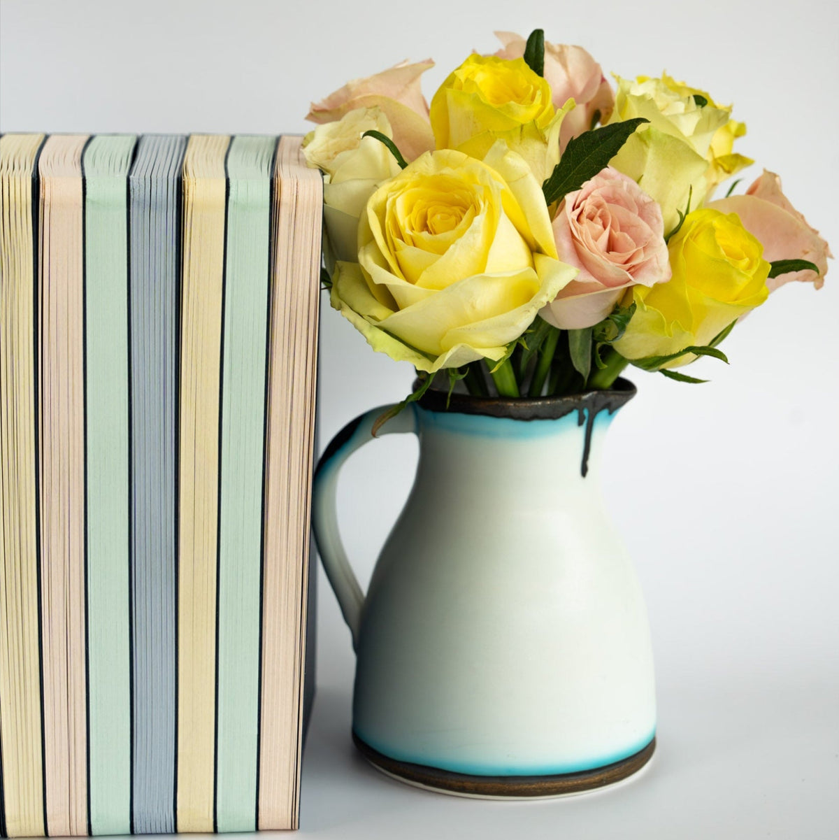 Vase with yellow and pink flowers next to a stack of The OakBook of all colours