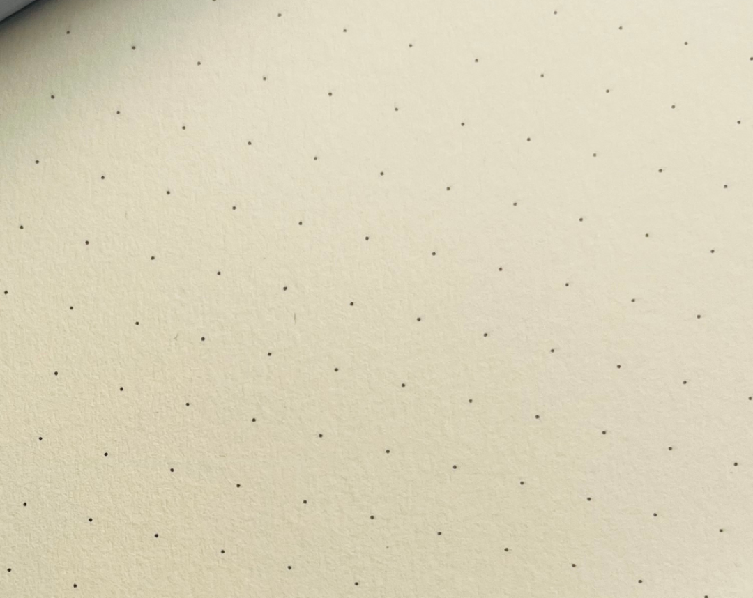 A close-up of a light yellow textured pagewith a uniform grid of tiny black dots.